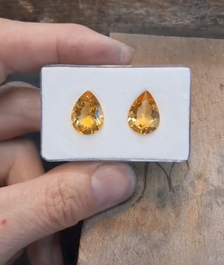A pair of yellow gemstone earrings in a white box held by a hand.