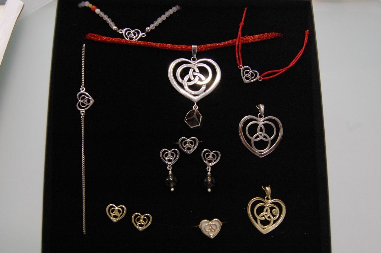 Eine Sammlung von silbernen und goldenen herzförmigen Anhängern und Ohrringen mit komplizierten Knotendesigns, auf schwarzem Hintergrund präsentiert.