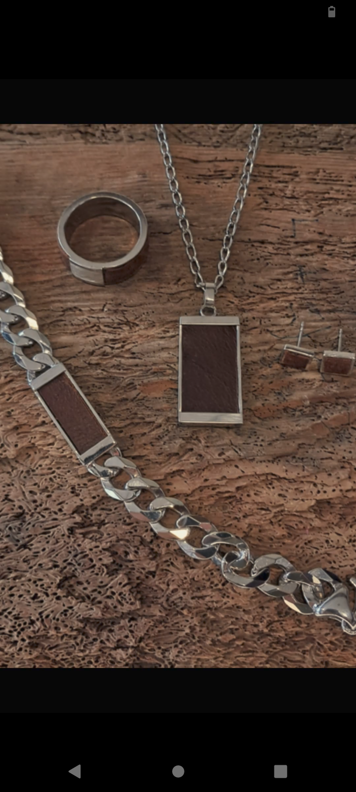 Ein Set aus Silberschmuck mit braunen Lederakzenten, bestehend aus einer Halskette, einem Armband und einem Paar Ohrringe, auf einer Holzoberfläche präsentiert.