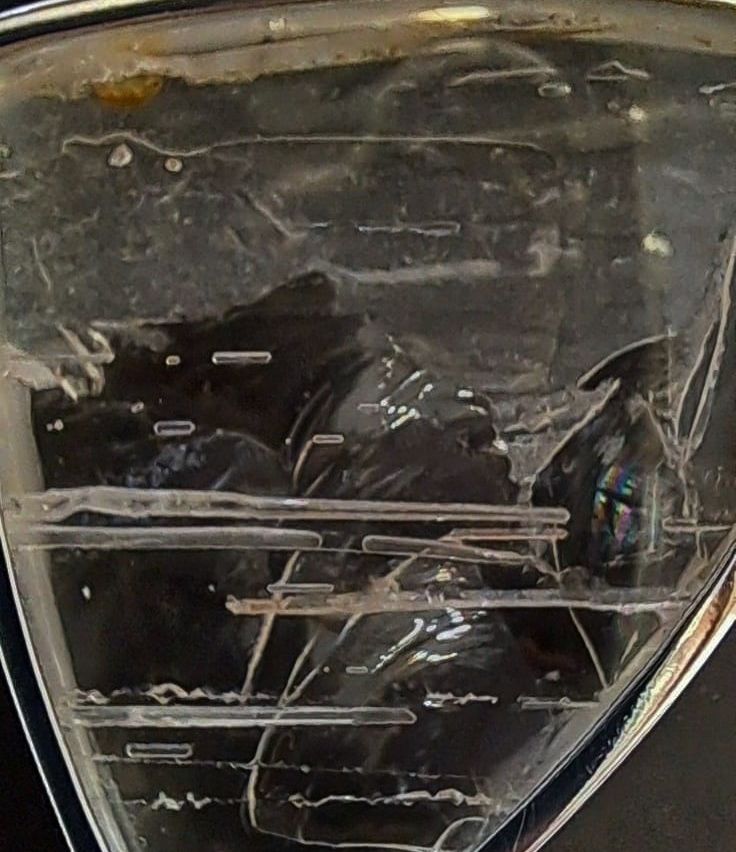Eine Nahaufnahme eines beschädigten Glasobjekts mit Rissen und einem Metallrahmen. Das Glas erscheint transparent mit etwas Schmutz und Ablagerungen.