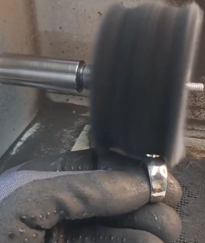 A hand holds a metal ring under a grinding wheel. The wheel spins rapidly, producing sparks. The metal ring is being shaped.