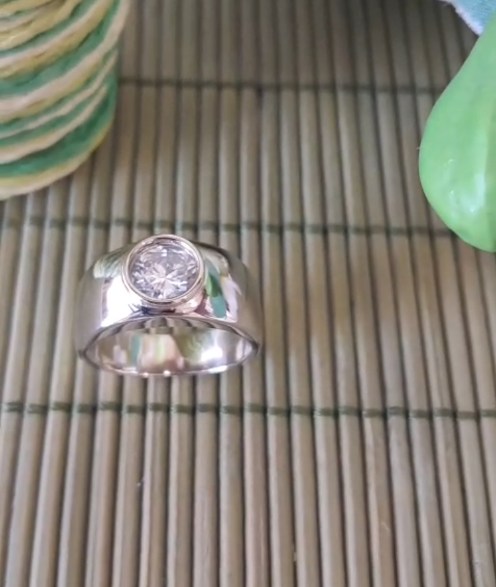 A silver ring with a single diamond on a bamboo mat. A stack of green and white cookies are on the left.
