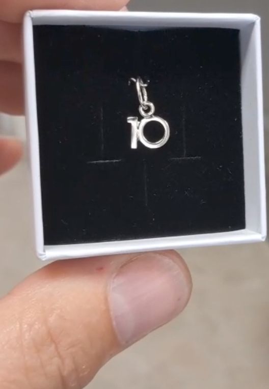 Eine Nahaufnahme eines Fingers, der eine weiße Schachtel mit einem silbernen Anhänger mit der Aufschrift 10 hält.