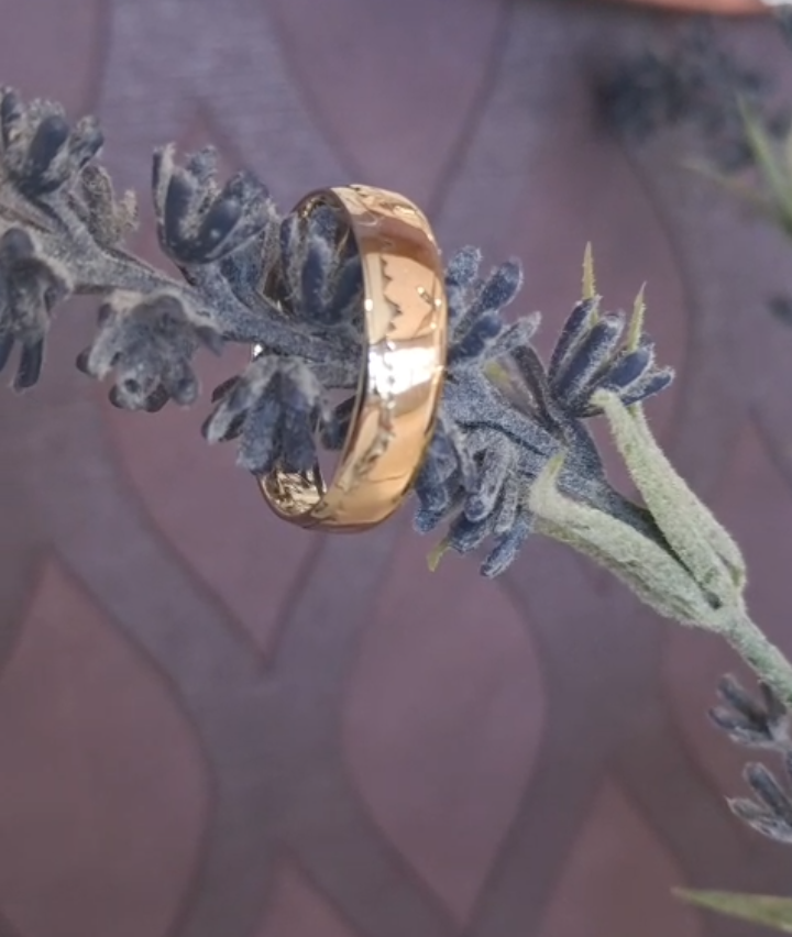 Ein Nahaufnahme eines goldenen Rings, der auf einer Lavendelpflanze ruht. Die Lavendelblüten sind lila und grün, und der Hintergrund ist leicht verschwommen.