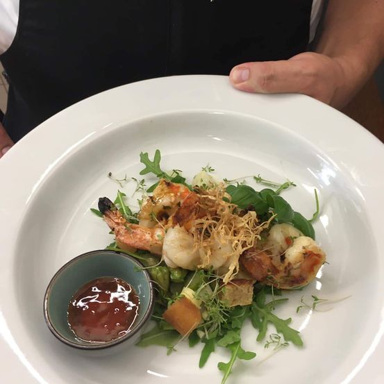 Ein weißer Teller mit Salat und Garnelen, mit einer kleinen Schüssel Sauce auf der Seite.