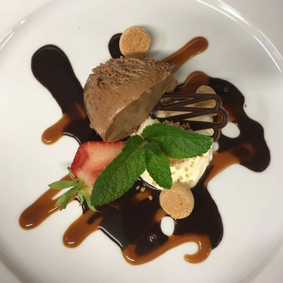 Ein weißer Teller enthält ein Schokoladen-Dessert mit Minzblättern und einer Erdbeere, überzogen mit Schokoladensauce.