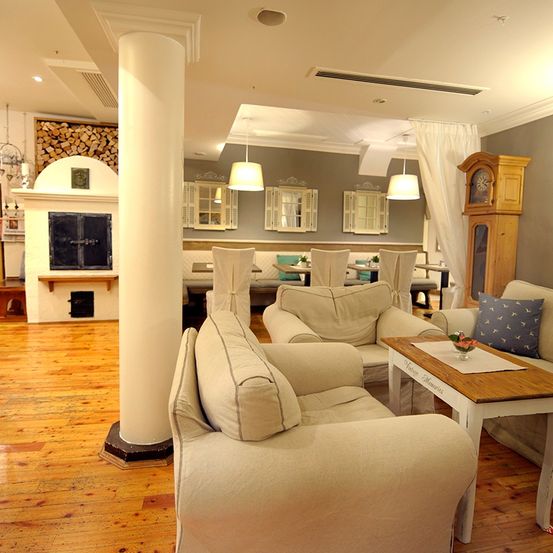 Ein elegantes Wohnzimmer mit Holzboden, weißen Möbeln und einem großen Kamin. Es verfügt über eine große Holzsäule, zwei Sofas und einen Tisch mit einer Blumenvase.