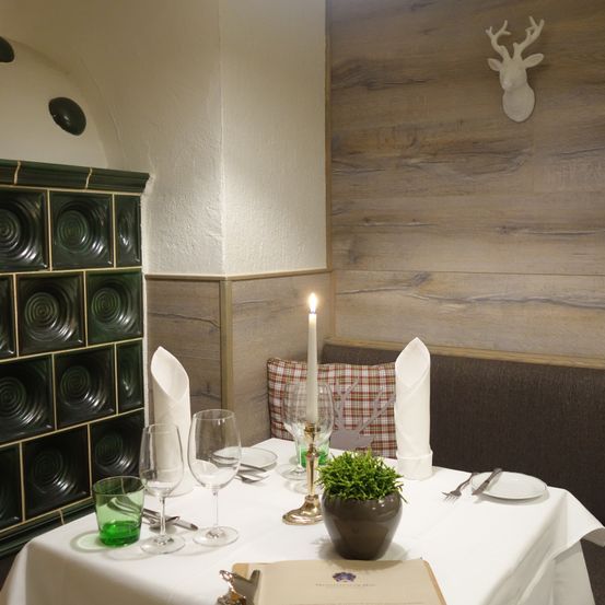 Ein elegant gedeckter Tisch mit Weingläsern und einer Kerze, vor einer Holzwand mit einem aufgehängten Hirschkopf.