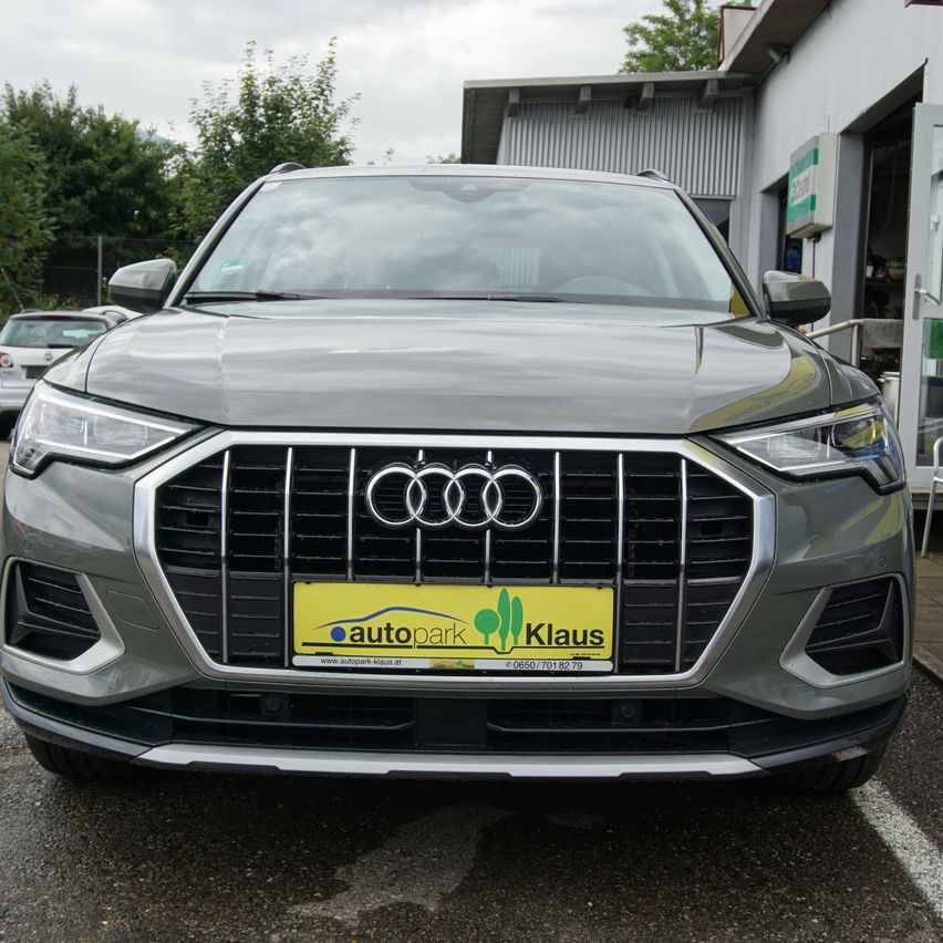 Ein grauer Audi SUV mit einem gelben Nummernschild, auf dem 'autopark Klaus' steht, ist vor einem Gebäude geparkt. Der Himmel ist bewölkt.