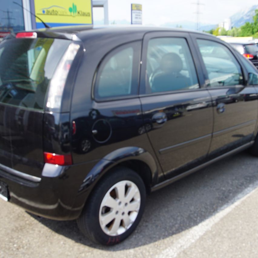 Ein schwarzer Wagen steht auf einem Parkplatz mit verschwommenem Hintergrund. Der hintere Teil des Autos ist sichtbar, einschließlich eines Ersatzreifens.