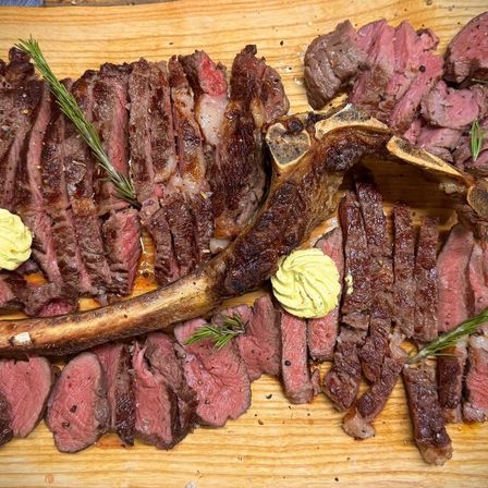 Ein Holzschneidebrett zeigt ein perfekt geschnittenes Rindersteak, garniert mit Rosmarin und einer Kelle cremiger Sauce.