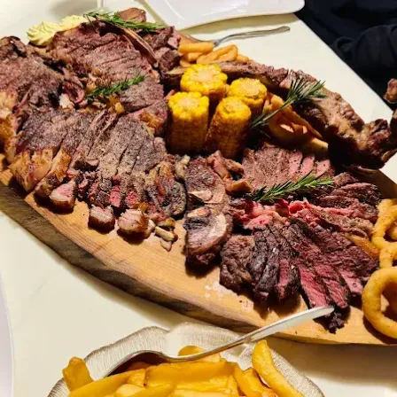 Ein Holztablett mit verschiedenen Fleischsorten, Maiskolben und Zwiebelringen.