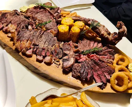 Ein Holztablett mit verschiedenen Fleischsorten, Maiskolben und Zwiebelringen.