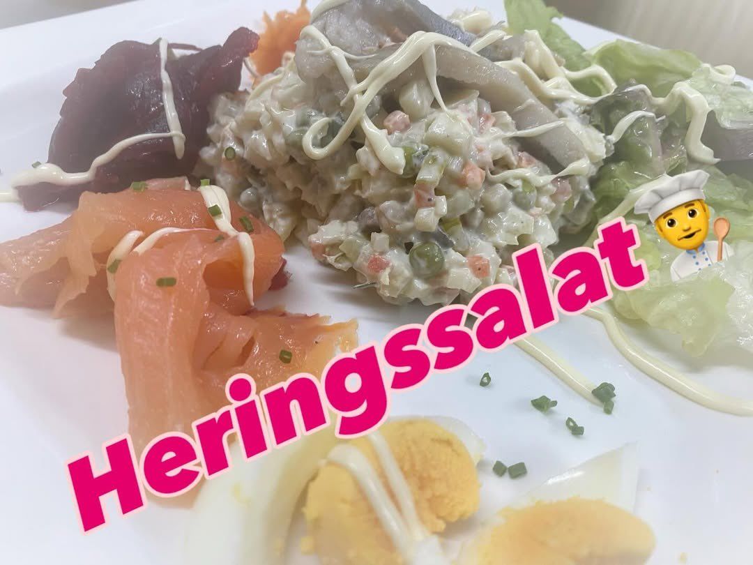 Ein Teller zeigt einen Salat mit weißer Sauce und Fisch, begleitet von geschnittenem Lachs und Eierhälften, garniert mit Kräutern und Karotten.
