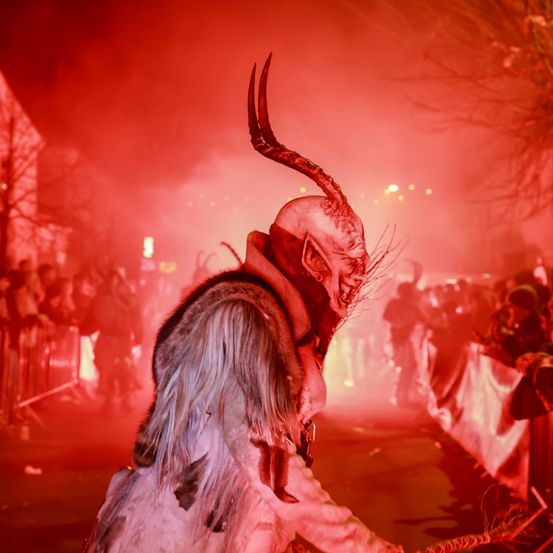 Eine Person in einem gehörnten Kostüm steht vor einer Menge bei roter Beleuchtung.