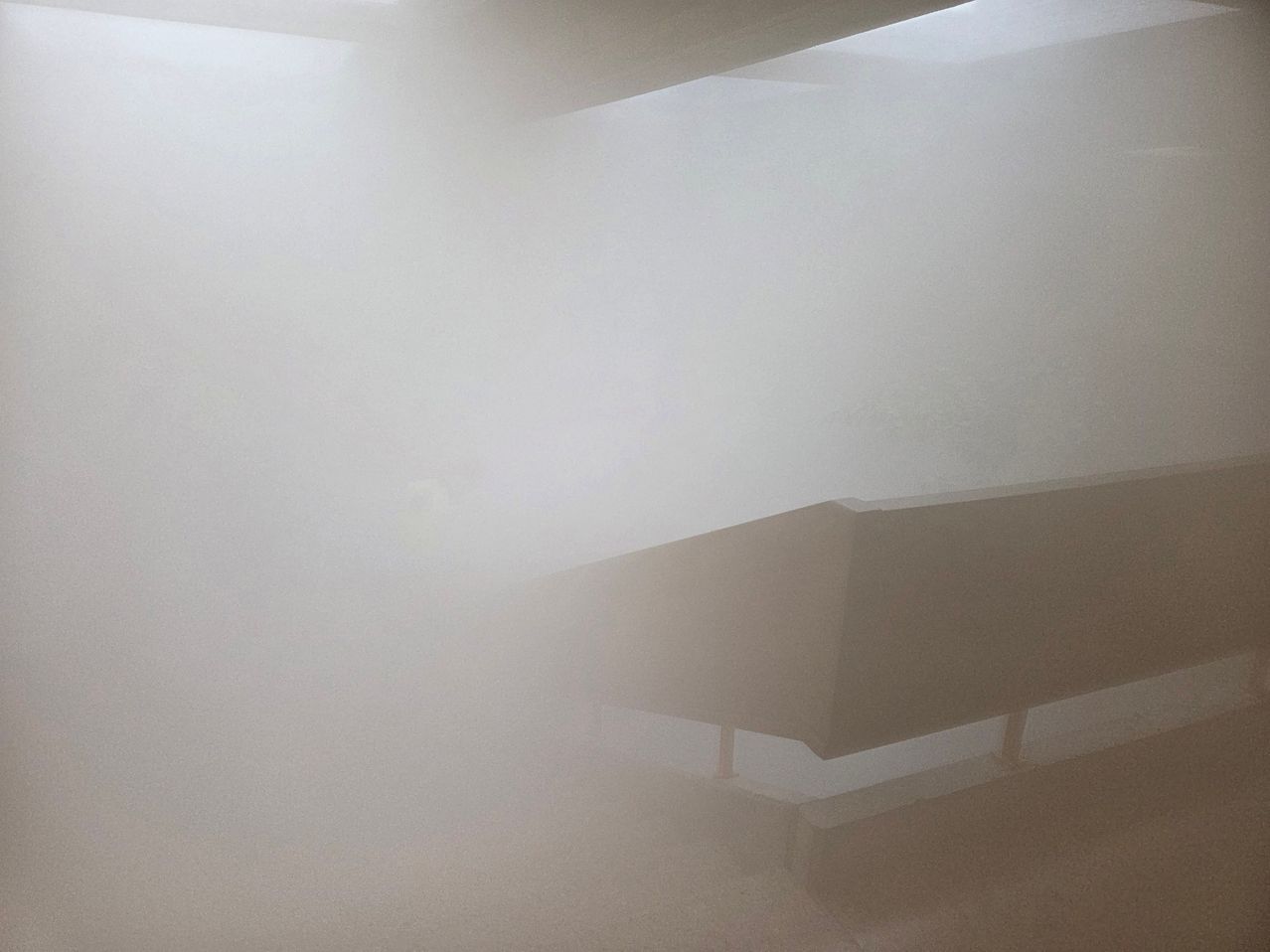A foggy image showing a part of a structure, possibly a bridge or a walkway, with a blurred background.