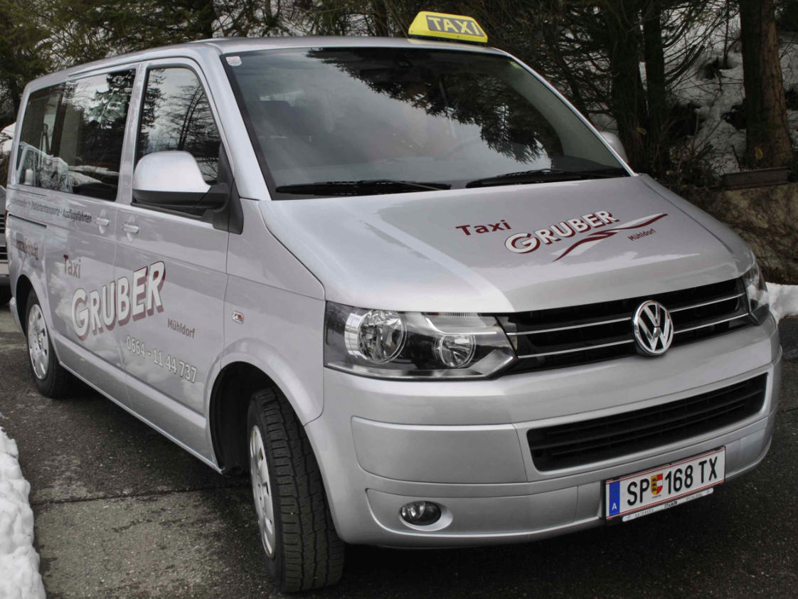 A silver Volkswagen taxi van with a yellow taxi sign on top is parked in a parking lot. The license plate reads 'SP 168'.