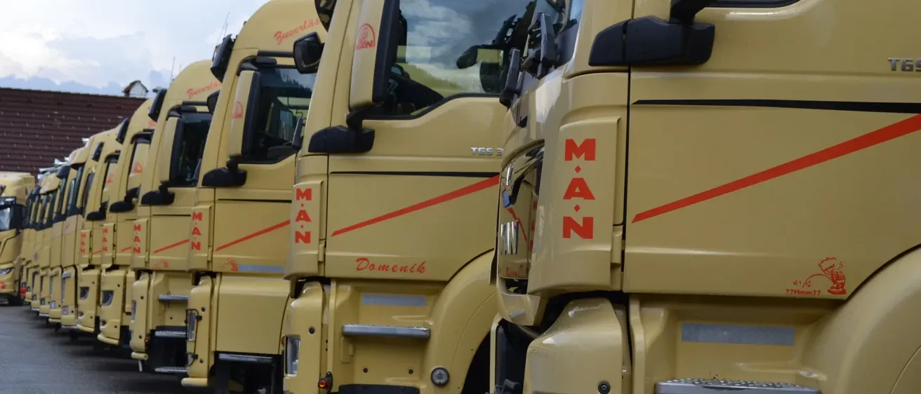 Eine Reihe gelber MAN-Lkw mit roten Streifen und dem Wort MAN auf der Front, die in einem Parkplatz geparkt sind.