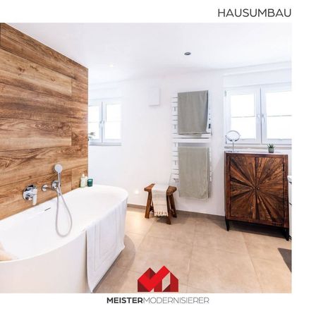 Ein modernes Badezimmer mit einer Holzwand, einer großen weißen Badewanne, einem Holzschrank und einem Handtuchhalter. Der Raum ist gut beleuchtet mit natürlichem Licht von den Fenstern.