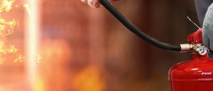 Nahaufnahme eines roten Feuerlöschers mit schwarzem Schlauch, der von einer Hand im Hintergrund gehalten wird.