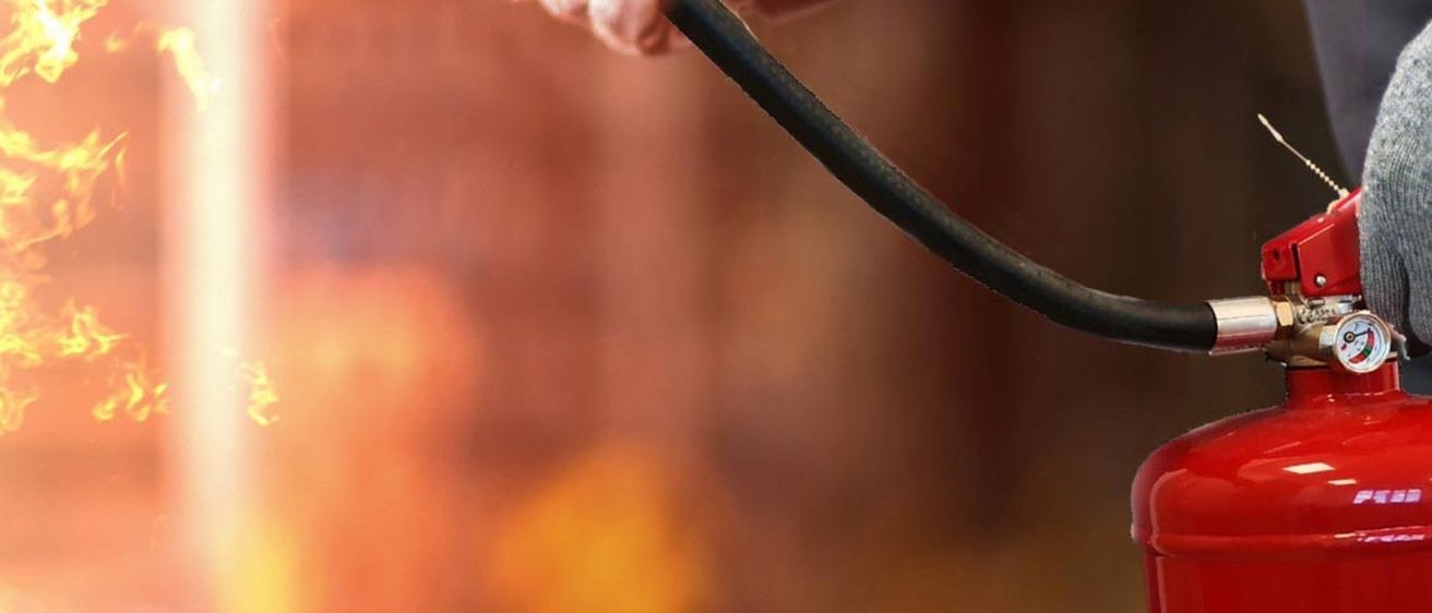 Nahaufnahme eines roten Feuerlöschers mit schwarzem Schlauch, der von einer Hand im Hintergrund gehalten wird.