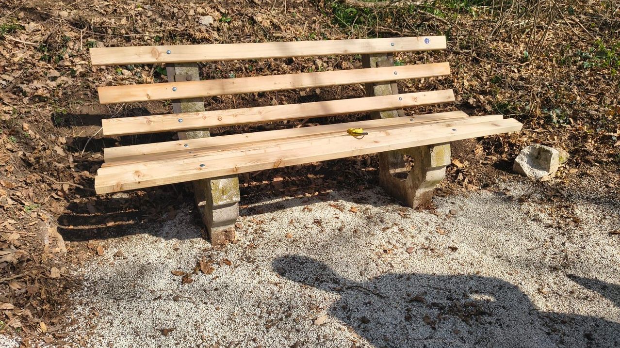 Eine Holzbank aus Kiefernholz steht auf einer Kiesoberfläche. Die Bank hat Metallschrauben an ihren Holzbrettern.