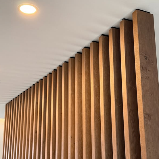 Eine Holzwand mit vertikalen Streifen. Die Wand besteht aus Eichenholz und hat eine hellbraune Farbe.