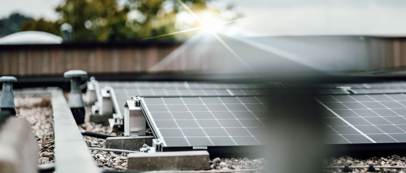 Solarmodule auf einem Dach, die Sonnenlicht einfangen und eine helle Reflexion im Vordergrund erzeugen.