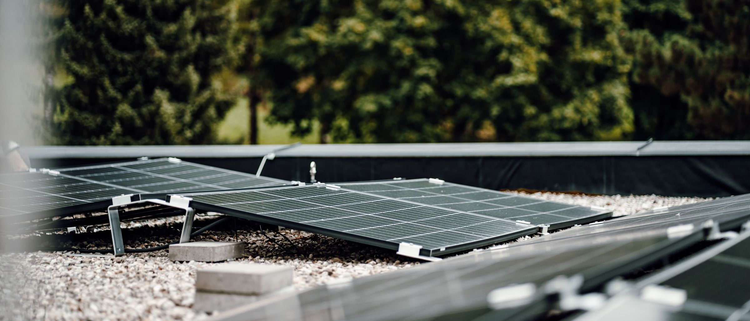 Eine Solarpanel-Installation auf dem Dach mit mehreren Paneelen auf einer Kiesfläche, umgeben von Bäumen.