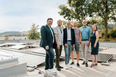 Eine Gruppe von sechs Personen, möglicherweise Kollegen, steht auf einem Dach mit Solarpanelen im Hintergrund und lächelt für ein Foto.