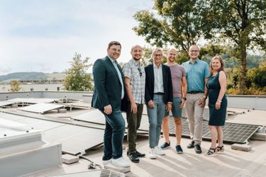 Eine Gruppe von sechs Personen, möglicherweise Kollegen, steht auf einem Dach mit Solarpanelen im Hintergrund und lächelt für ein Foto.