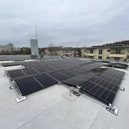 Ein Dach, das mit Solarpanelen bedeckt ist, umgeben von Gebäuden unter einem bewölkten Himmel.
