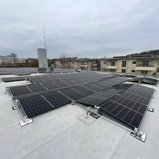 Ein Dach, das mit Solarpanelen bedeckt ist, umgeben von Gebäuden unter einem bewölkten Himmel.