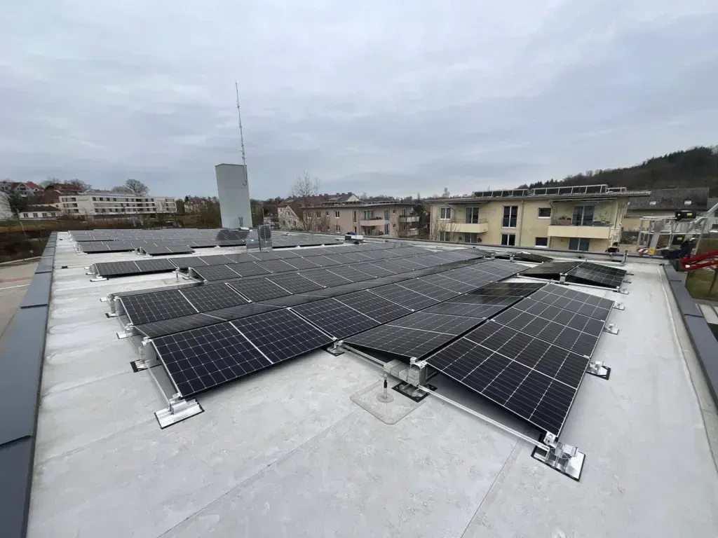 Ein Dach, das mit Solarpanelen bedeckt ist, umgeben von Gebäuden unter einem bewölkten Himmel.