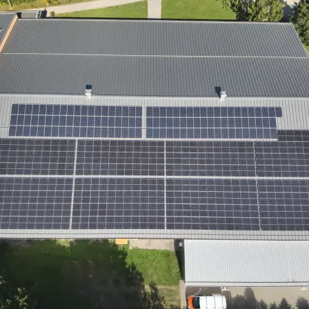 Eine Draufsicht auf ein Gebäude mit einem grauen Dach, das mit Solarpanelen bedeckt ist. Die Panels sind ordentlich in Reihen angeordnet.