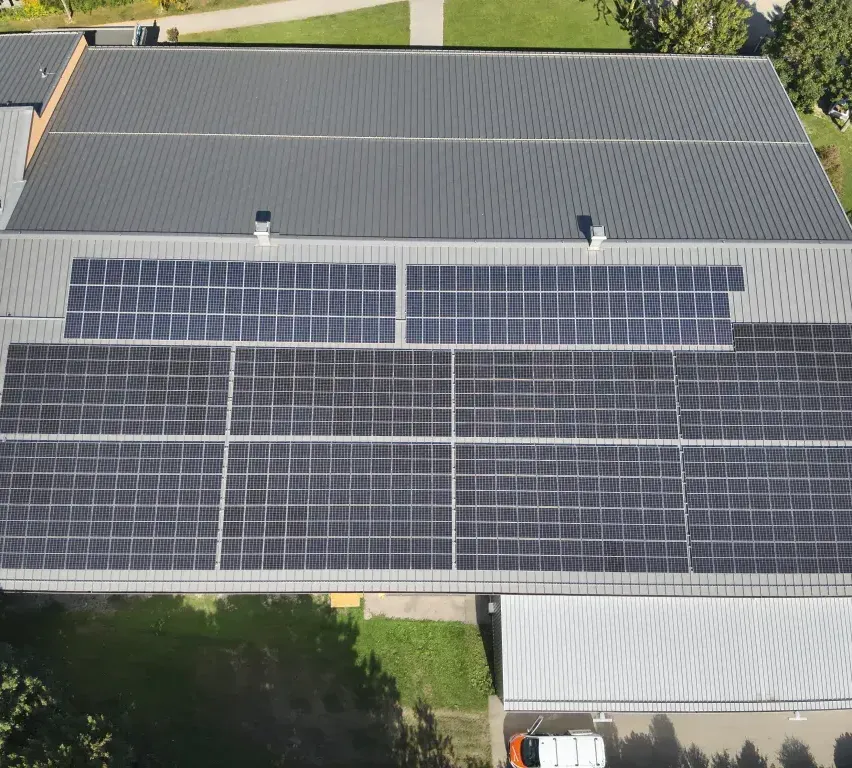 Eine Draufsicht auf ein Gebäude mit einem grauen Dach, das mit Solarpanelen bedeckt ist. Die Panels sind ordentlich in Reihen angeordnet.
