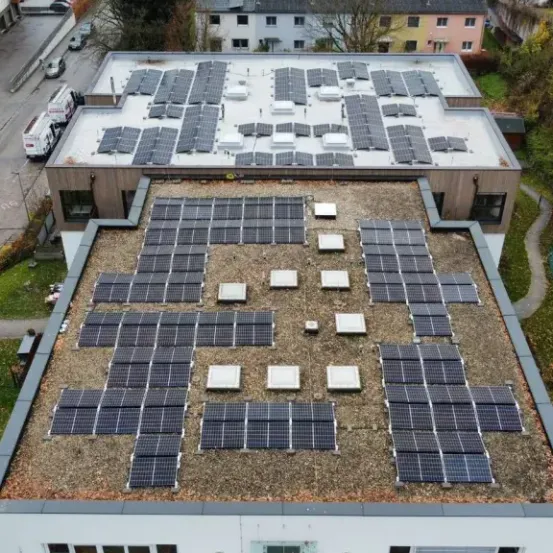 Eine Draufsicht auf ein Gebäude mit einem mit Solarmodulen bedeckten Dach. Das Gebäude ist von einem Parkplatz und einer Rasenfläche umgeben.