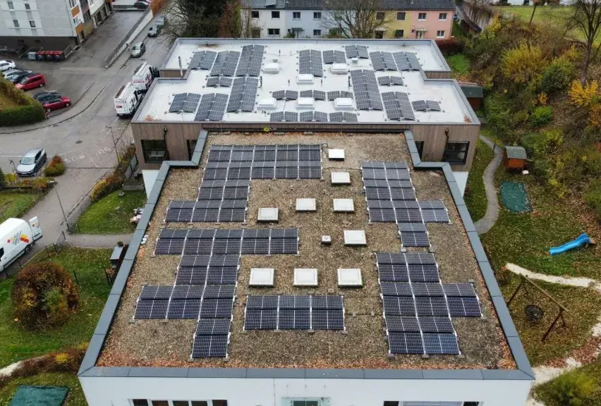 Eine Draufsicht auf ein Gebäude mit einem mit Solarmodulen bedeckten Dach. Das Gebäude ist von einem Parkplatz und einer Rasenfläche umgeben.