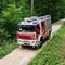 Ein Feuerwehrfahrzeug namens Maria Schutz, mit Feuerwehrleuten im Inneren, fährt auf einem Feldweg im Wald.