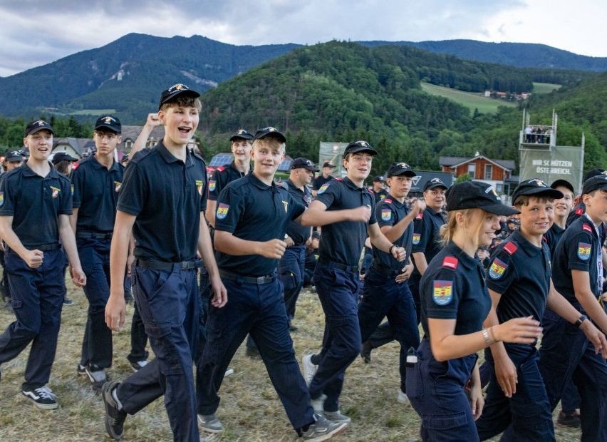A group of young people in uniform run across a field with mountains in the background.