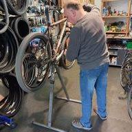 Ein Mann repariert ein Fahrrad in einem Fahrradgeschäft mit vielen Fahrrädern und Reifen an der Wand.