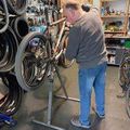 Ein Mann repariert ein Fahrrad in einem Fahrradgeschäft mit vielen Fahrrädern und Reifen an der Wand.