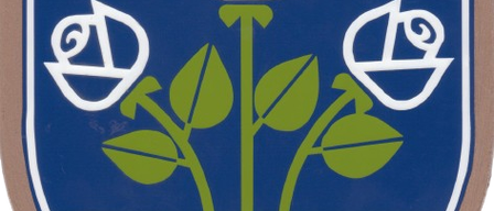 Ein blauer Schild mit weißem Rand, der drei weiße Rosen auf grünem Hintergrund enthält. Zwei weiße Pluszeichen befinden sich in den oberen Ecken.