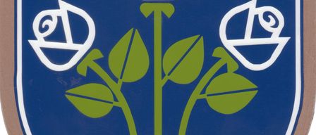 Ein blauer Schild mit grüner Basis und drei weißen Rosen darauf. Zwei silberne Kreuze sind über den Rosen.