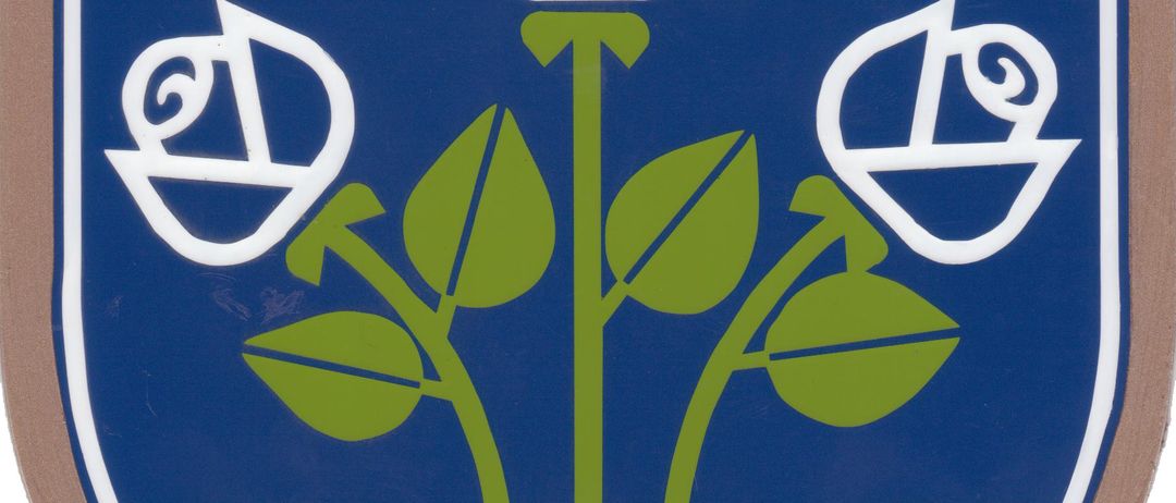 Ein blauer Schild mit grüner Basis und drei weißen Rosen darauf. Zwei silberne Kreuze sind über den Rosen.