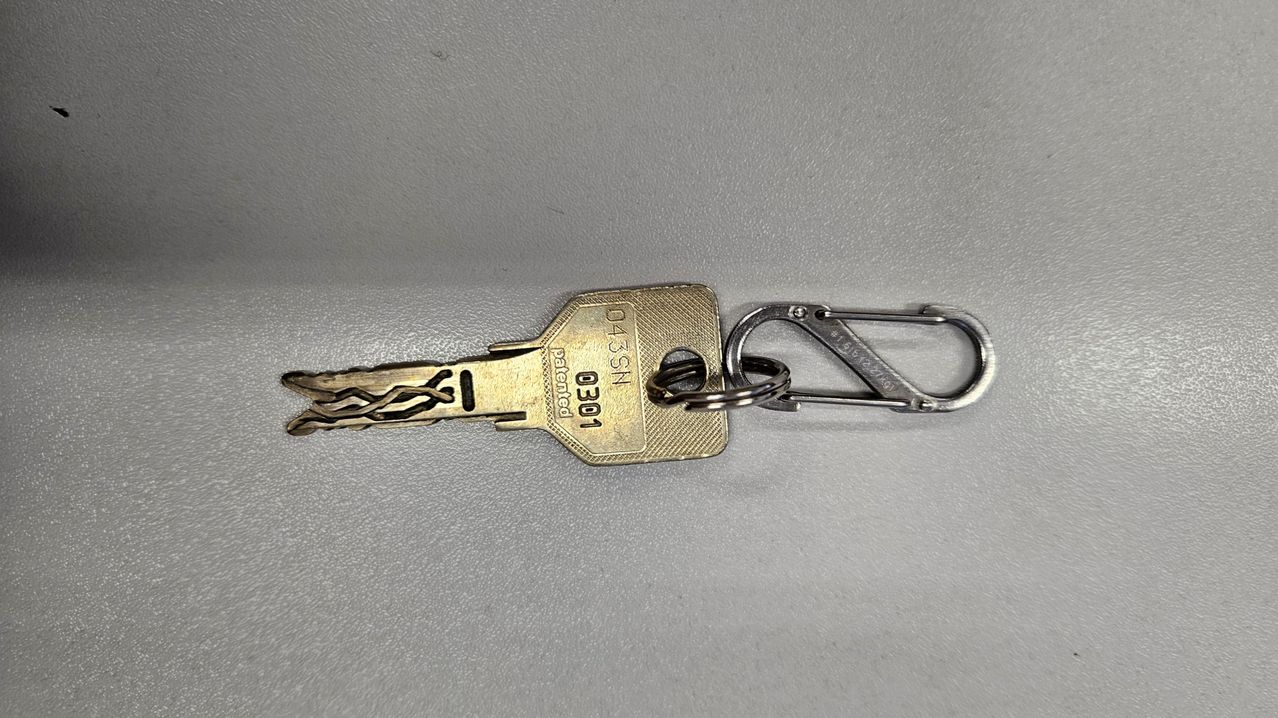 Ein goldener Schlüsselanhänger mit einem Schlüssel, der mit 0301 gekennzeichnet ist, befestigt an einem silbernen Karabiner. Der Schlüssel ist als patentiert gekennzeichnet und hat ein einzigartiges Design.