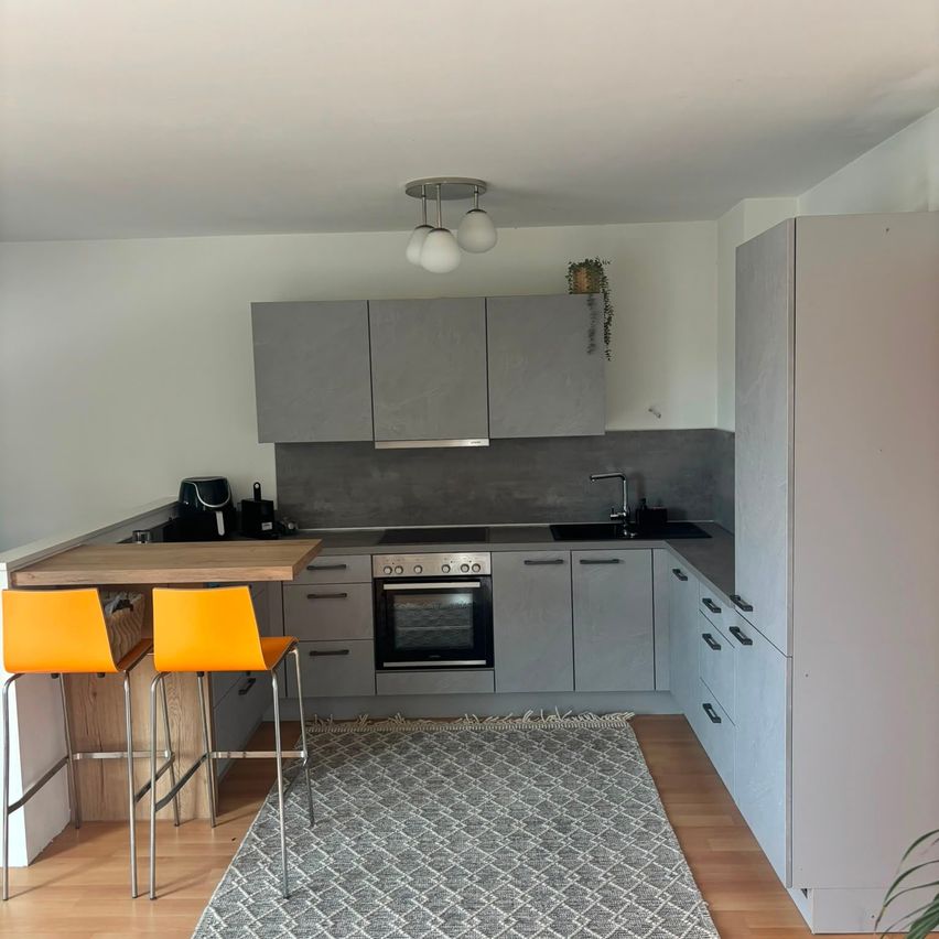 A modern kitchen with gray cabinets, a wooden countertop, and yellow chairs. The room features a ceiling lamp, a sink, and a stove.