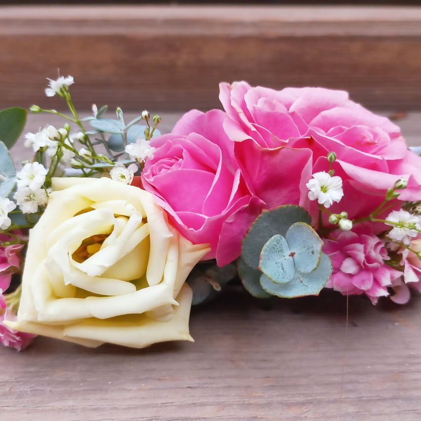 Eine Nahaufnahme einer Blumenarrangement mit rosa Rosen, einer weißen Rose und grünen Blättern auf einer Holzoberfläche.