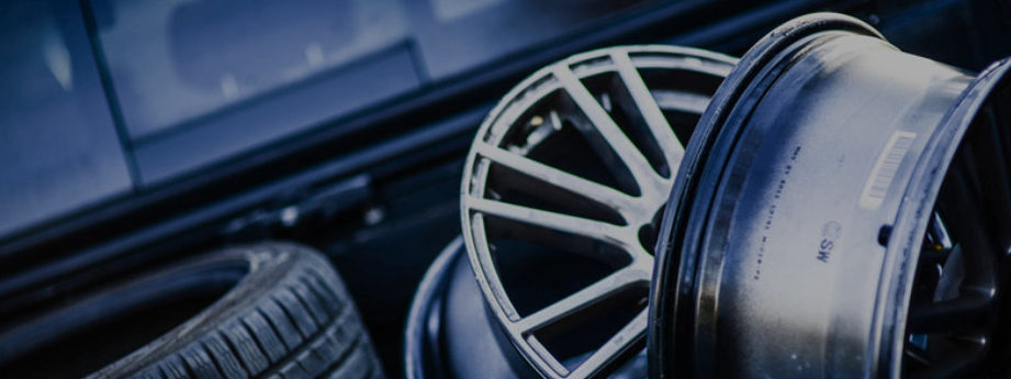 Nahaufnahme von Leichtmetallrädern mit einem Reifen auf der linken Seite, mit glänzendem Finish und sichtbaren Speichen, vor einem unscharfen Hintergrund.