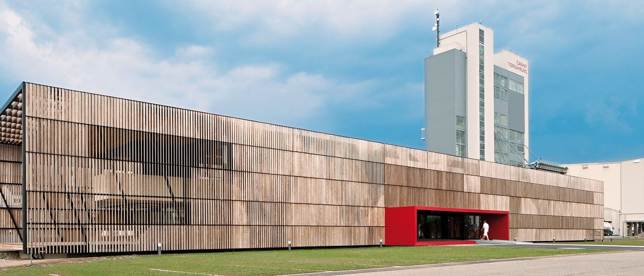 Ein modernes Gebäude mit einer Holzfassade und einem roten Eingangskasten an einem sonnigen Tag.